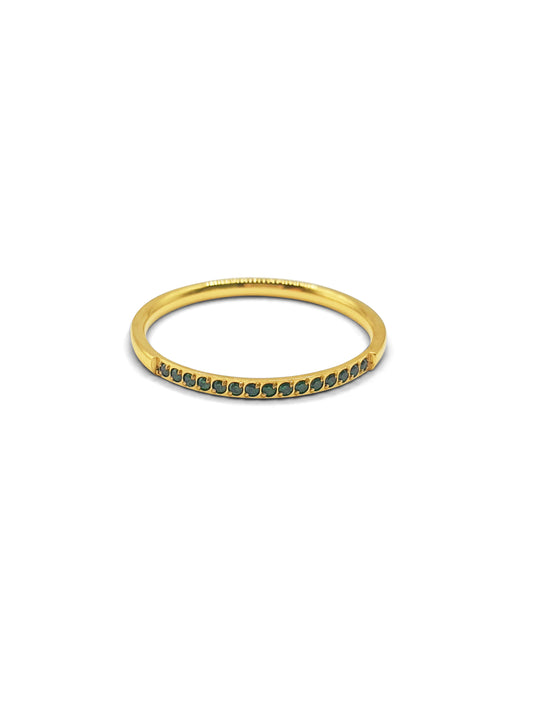 A gold stackable band ring set at the top with small green gems sits against a white background