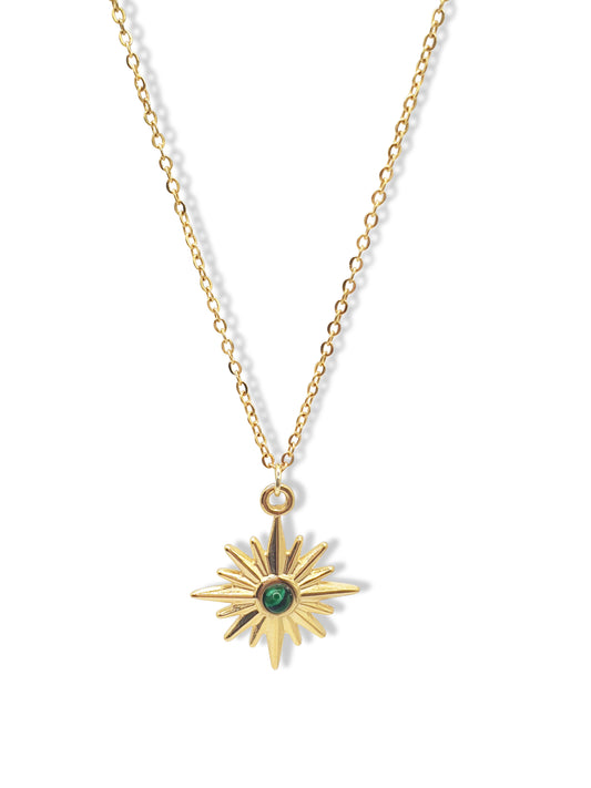 A gold necklace with a star shaped pendant set in the middle with a green  gem hangs against a white background