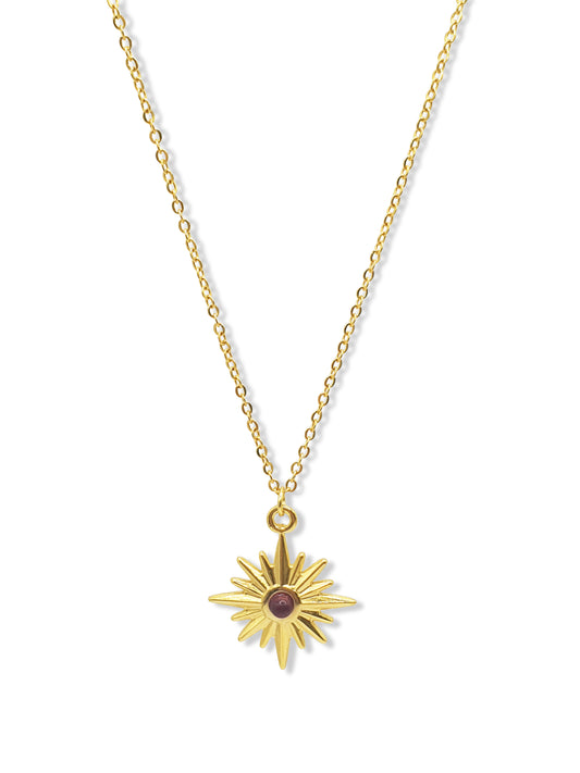 A gold necklace with a star shaped pendant set in the middle witha  red gem hangs against a white background