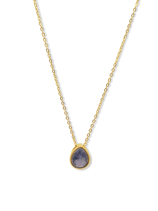 A gold necklace with a teardrop pendant set with a purple stone hangs against a white background