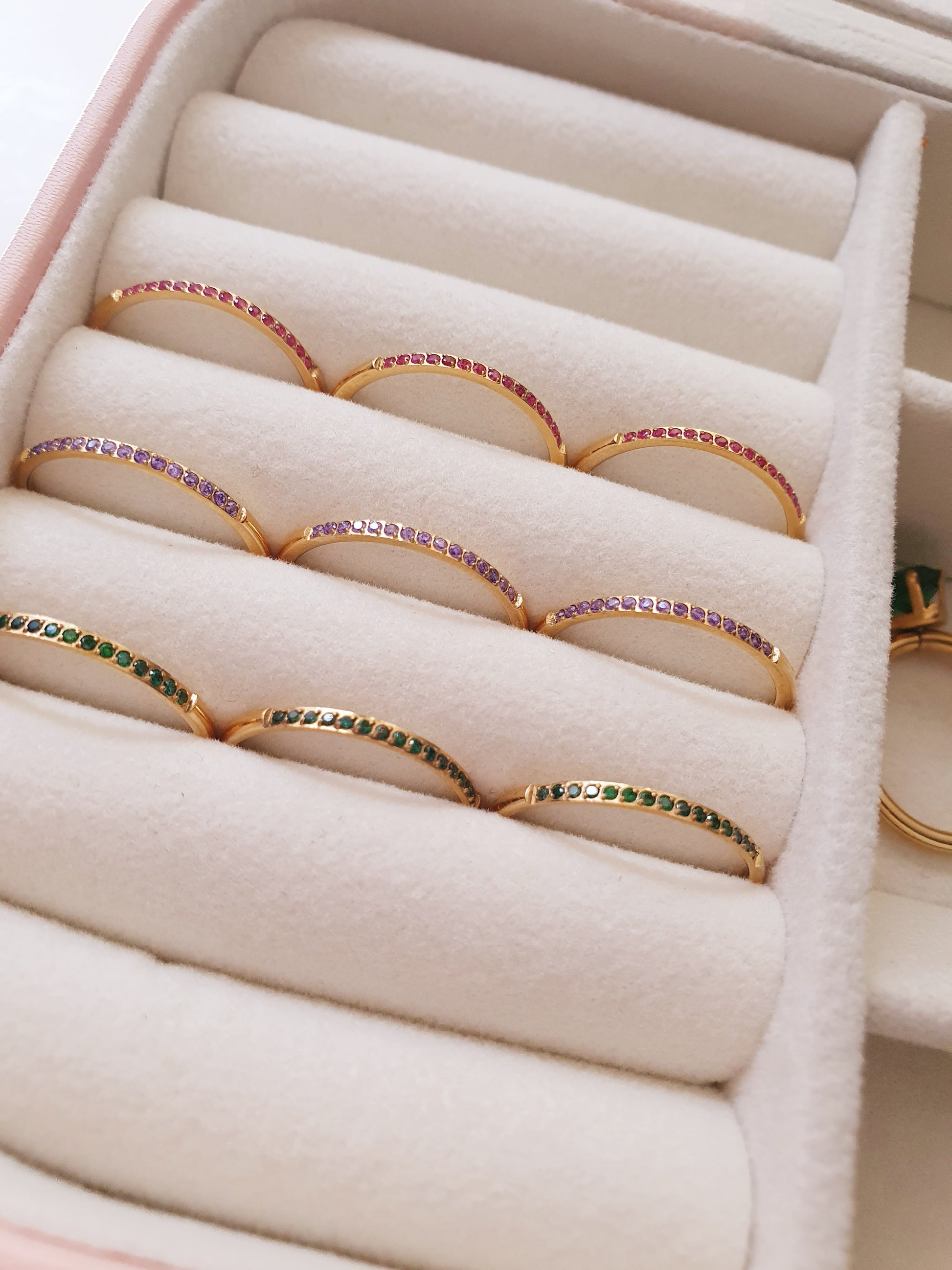 A jewellery box holds nine gold rings partially set with either green, purple or pink stones