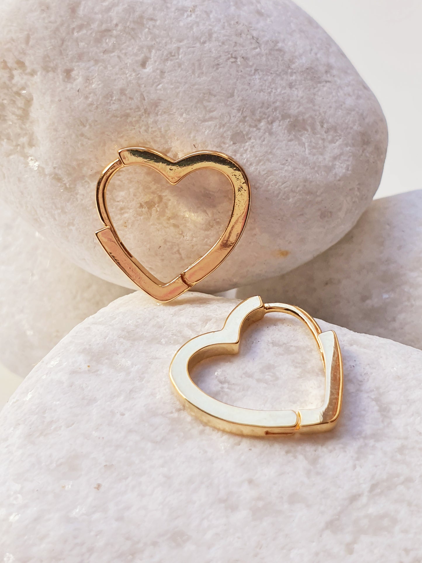 A pair of gold heart shaped huggies sit against white stones