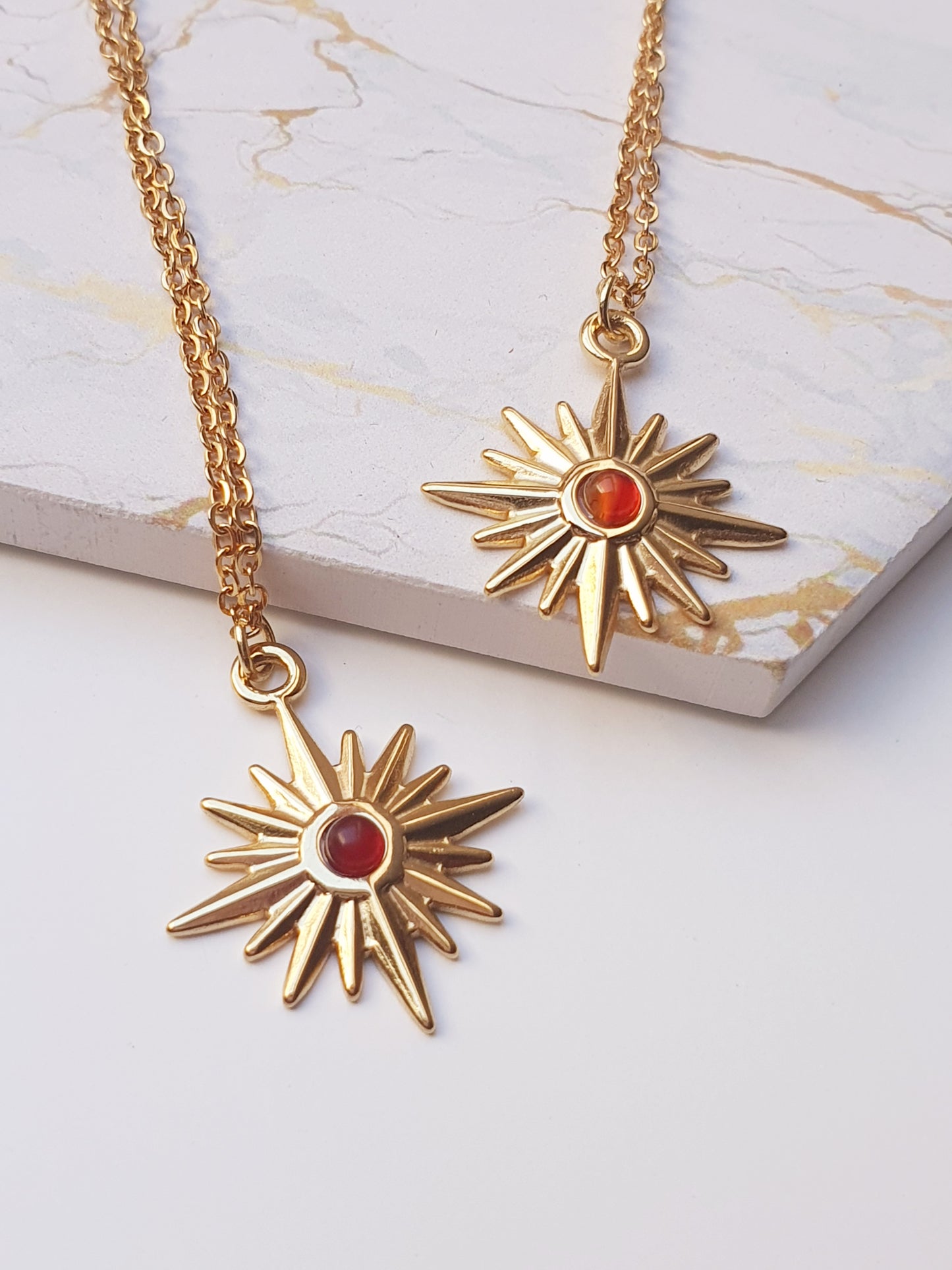 Two gold necklaces with star shaped pendants set in the middle with a small red gem rest on a coaster