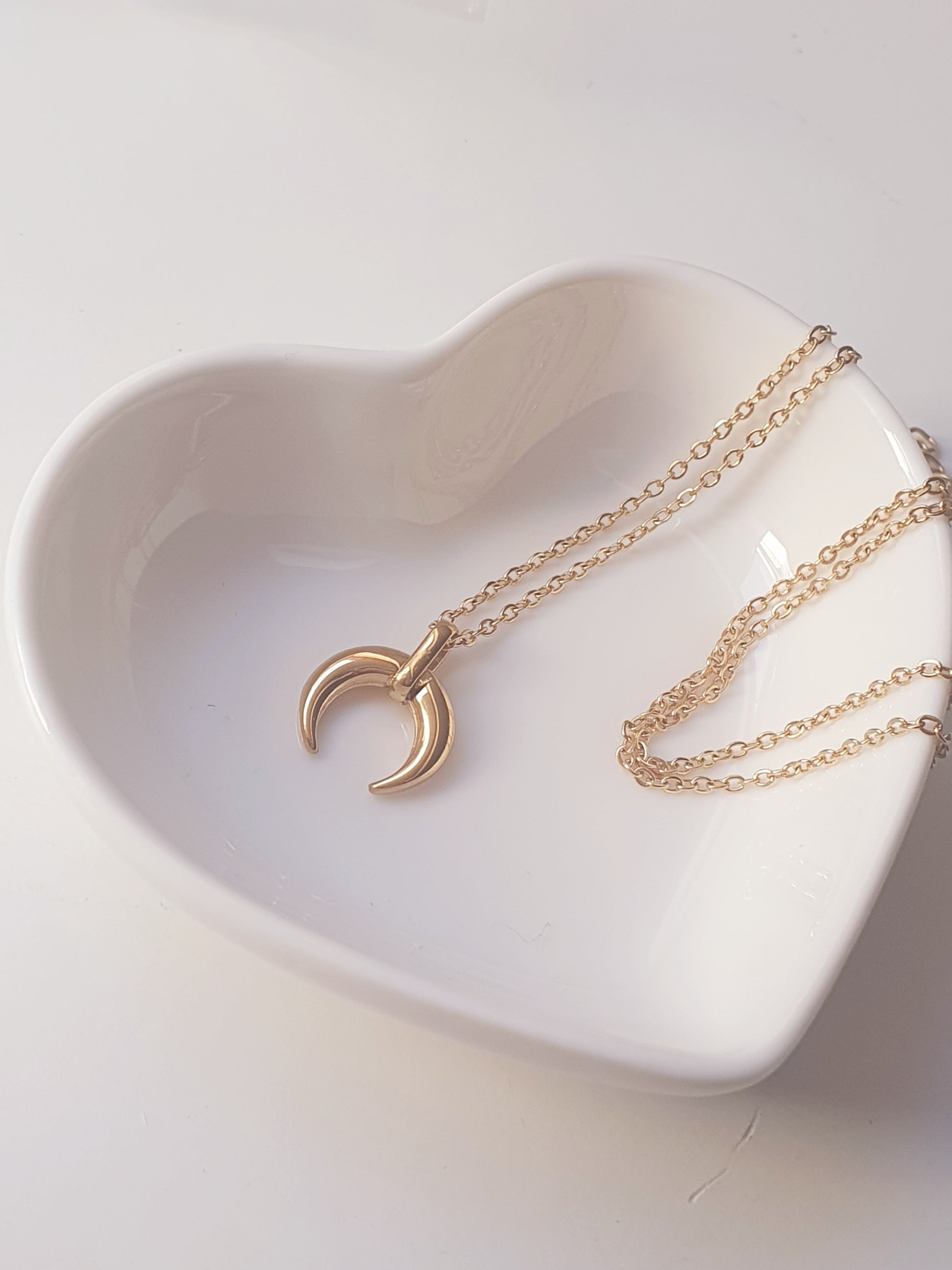  necklace with a crescent moon pendant rests on a white heart shaped dish