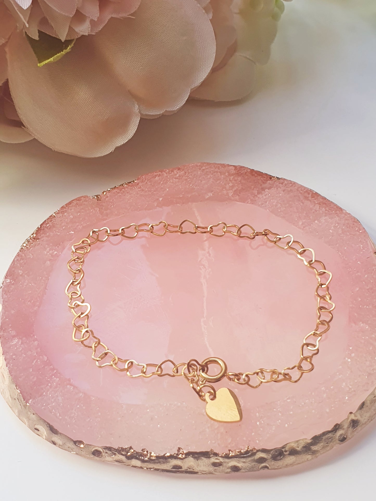 Gold bracelet made up of heart shaped links and fastened with a spring loaded clasp, resting on pink agate