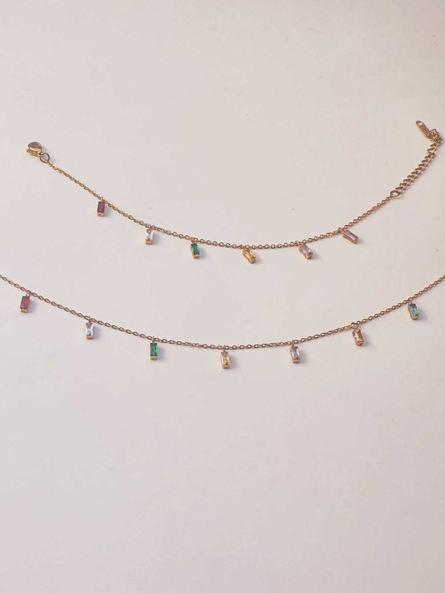 A dainty gold necklace with dangling gems in multiple colours and a matching bracelet above it