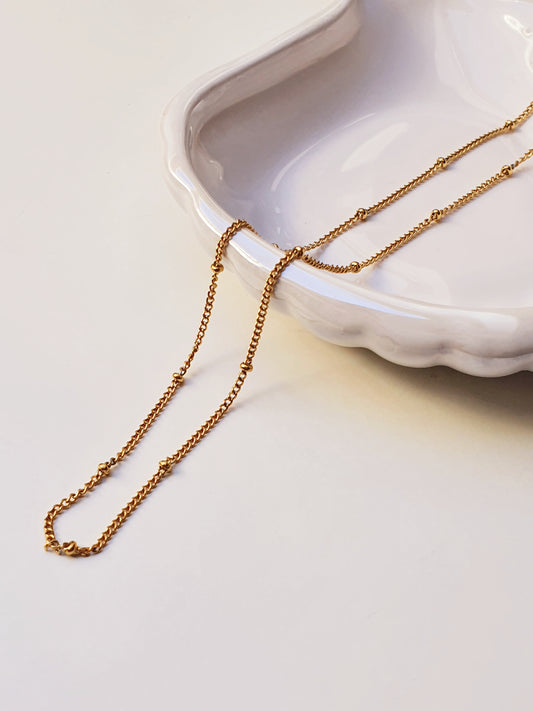 A gold satellite chain rests in a white shell shaped dish