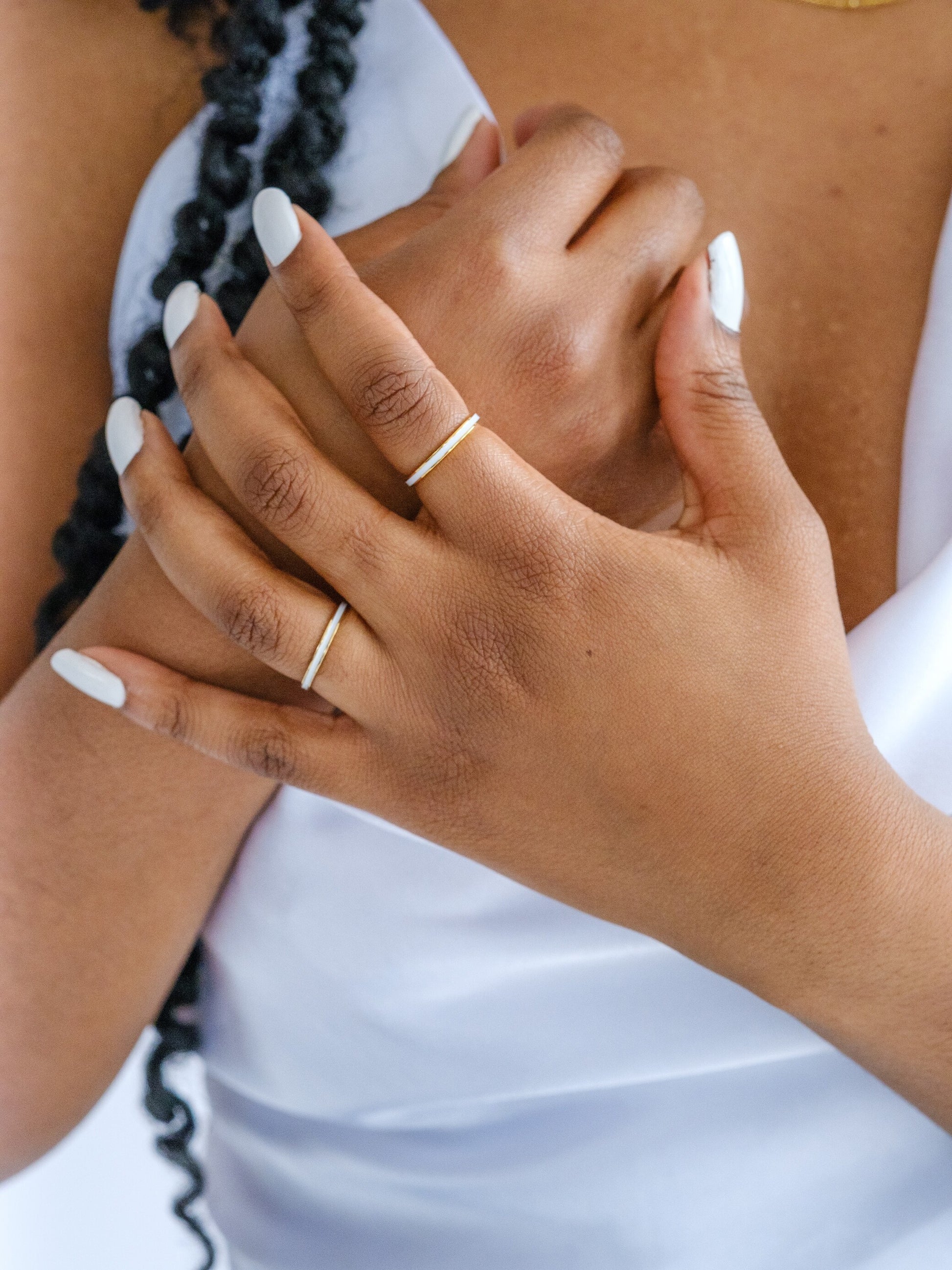A woman's hand wears two gold band rings with white enamel banding around the middle