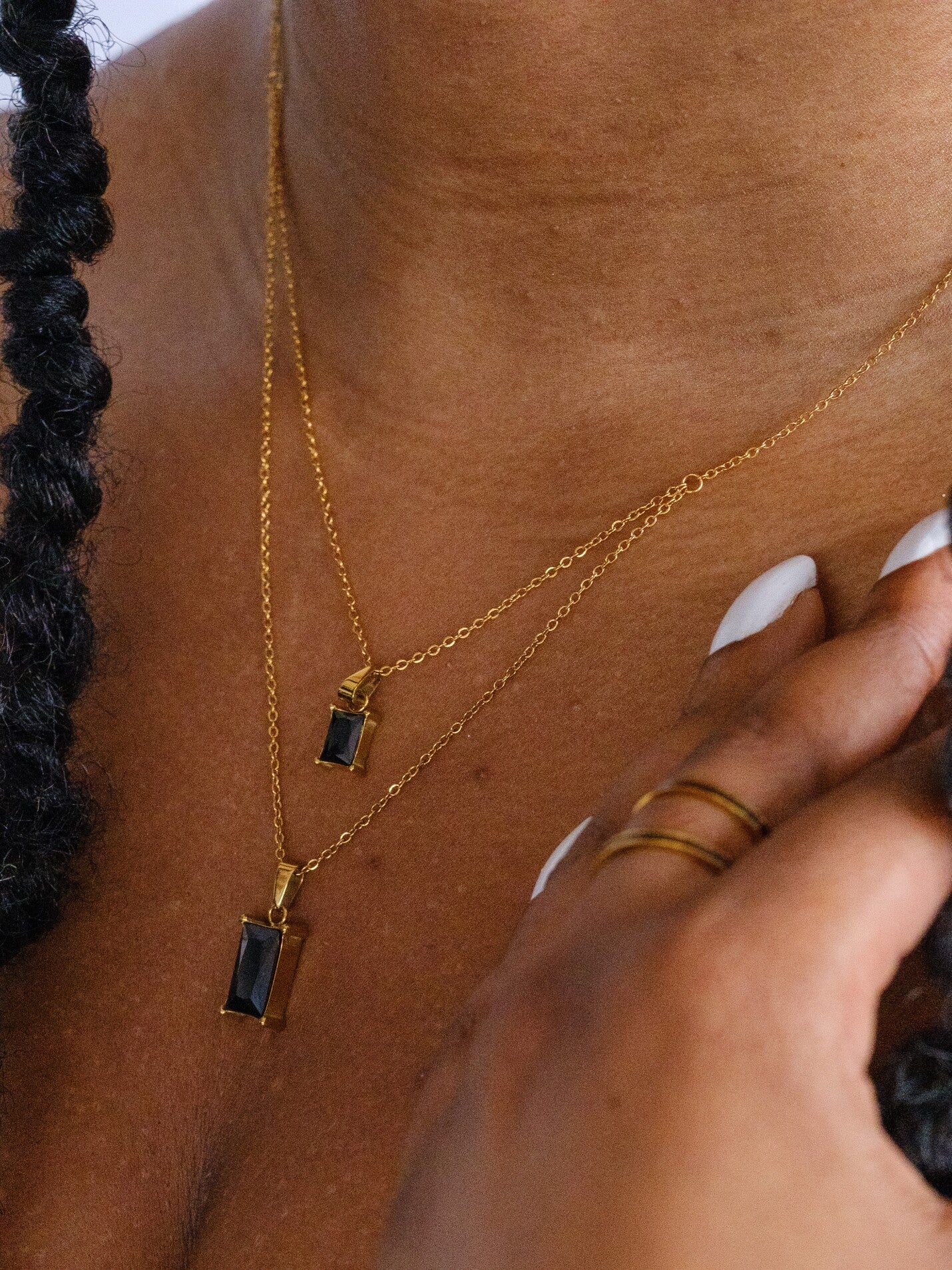 Woman's neck wearing a double layered necklace with two black rectangle jewel pendants
