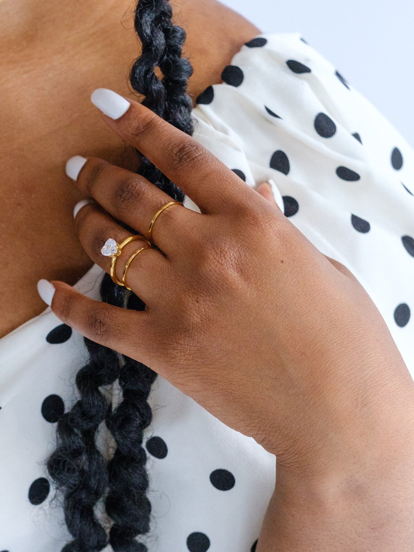 Woman's hand wearing 3 gold rings. Two rings are slim gold stacking bands. One ring is set with a clear heart gem stacked with  one of the gold bans