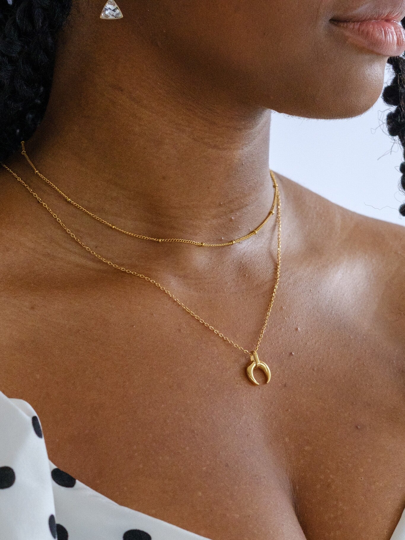 A woman wears a gold satellite chain and a loner necklace with a crescent moon pendant