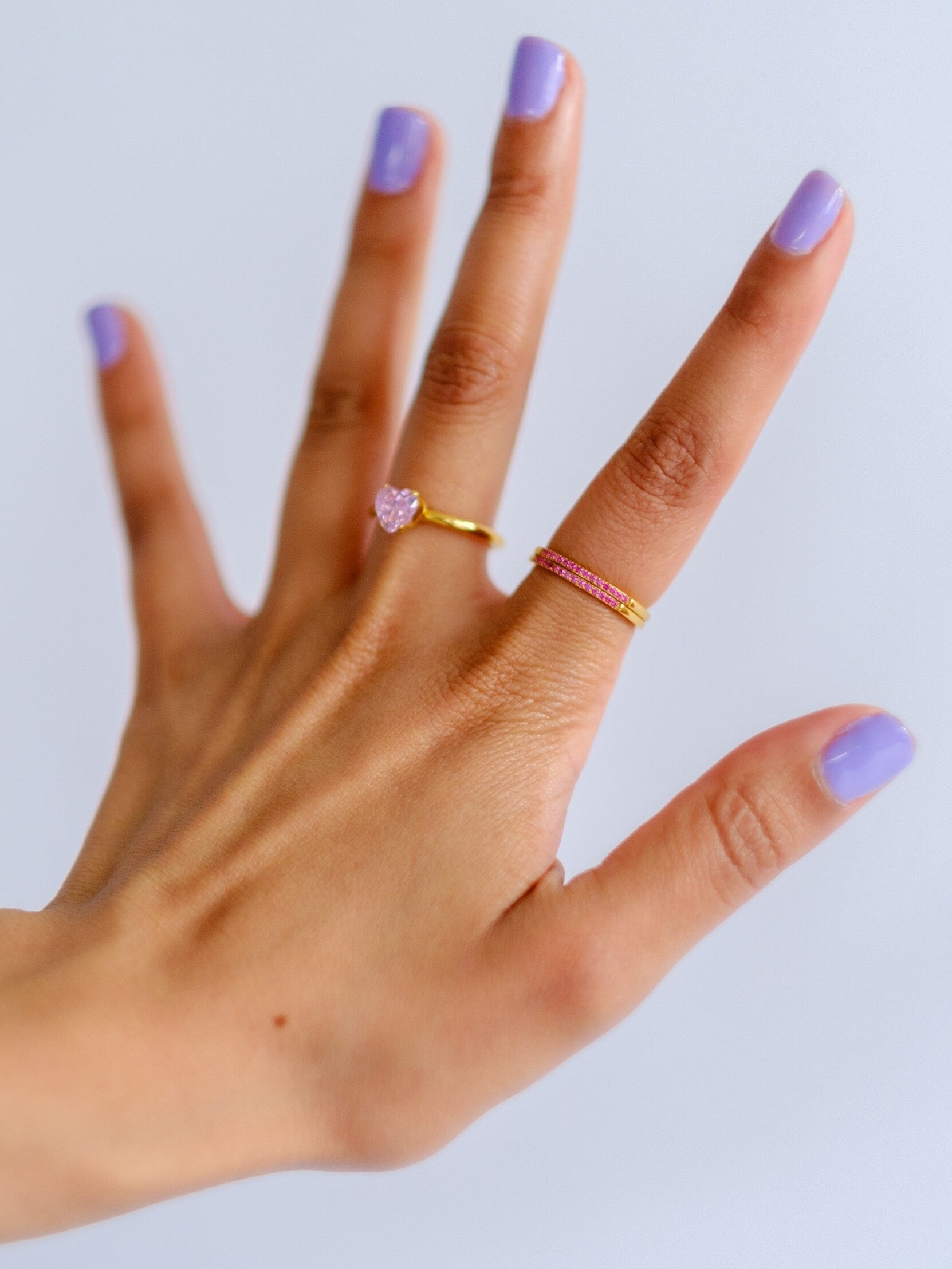Woman's hand wearing three gold rings in two different styles, set with pink stones