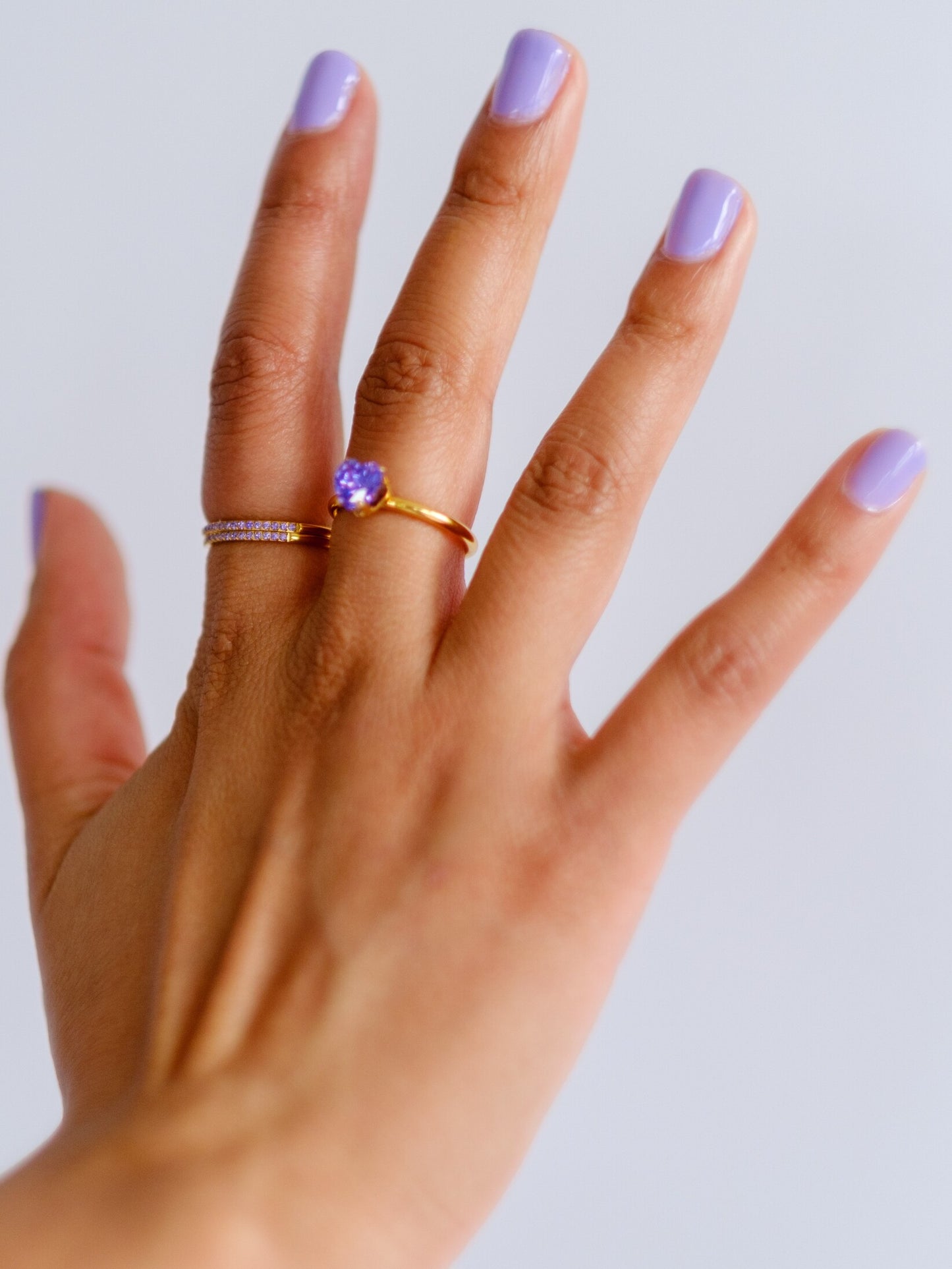 Woman's hand wearing three gold rings in two different styles, set with purple stones