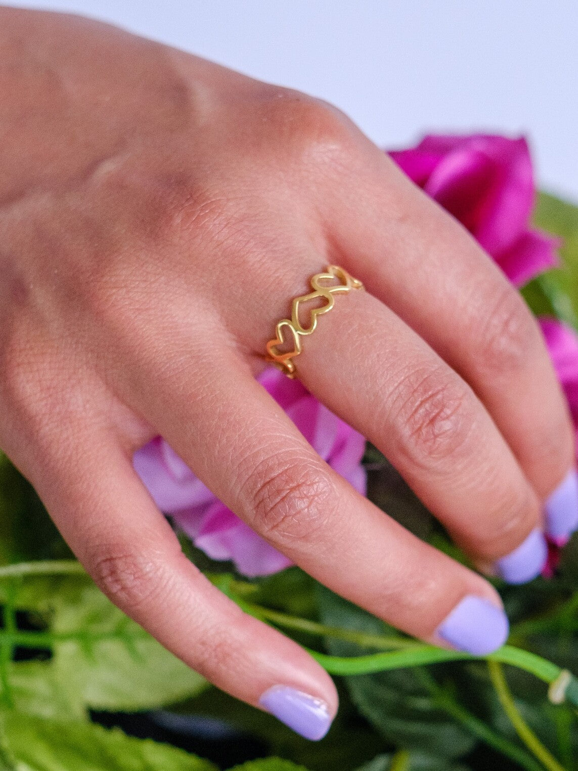 A woman's hand rests on flowers and wears a gold ring made up of connected stencil hearts