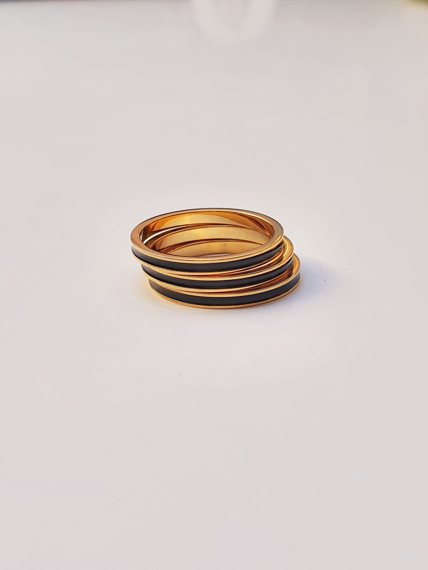 Three gold band rings with black enamel banding around the middle are stacked on top each other against a white background