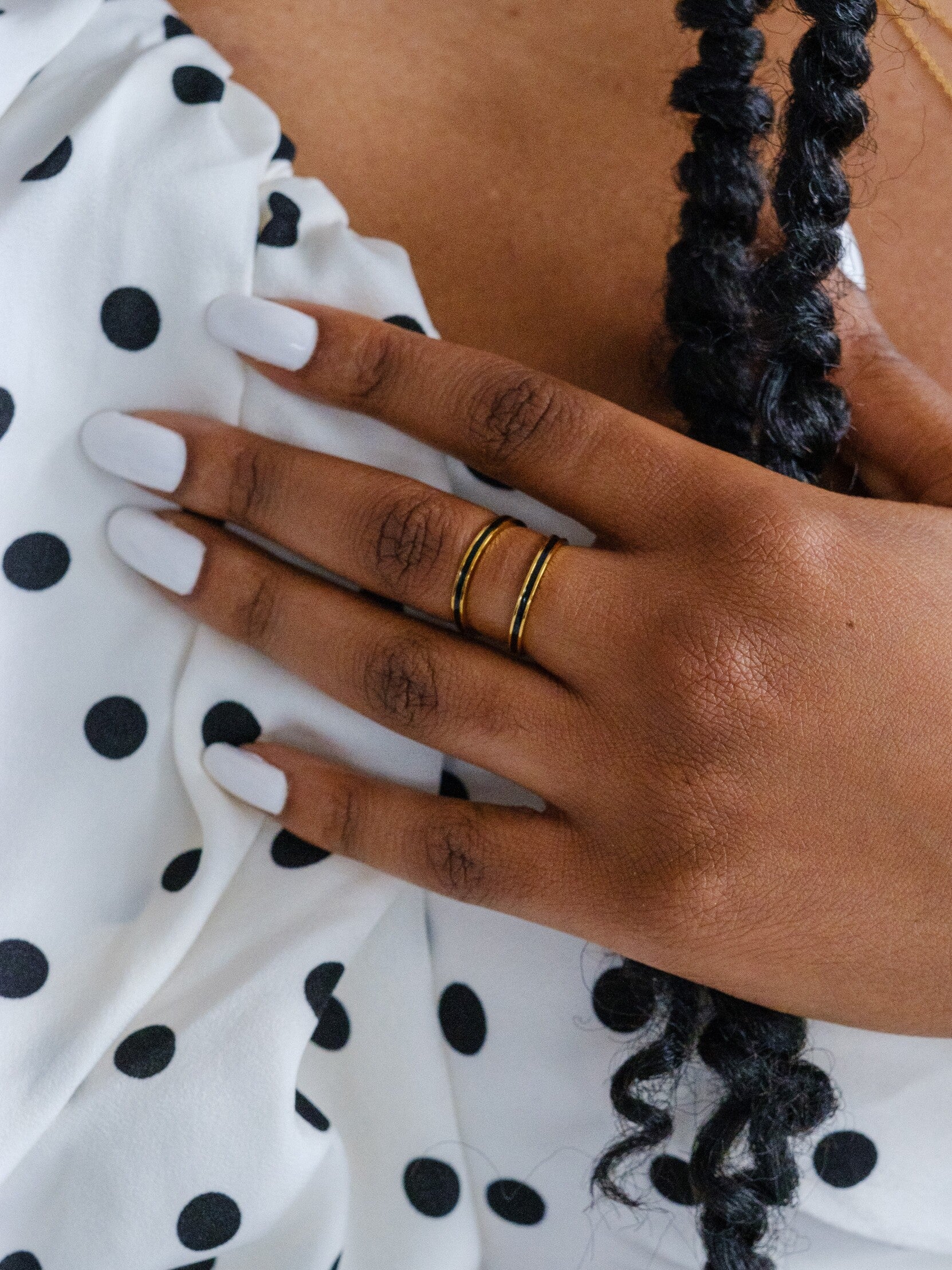 A woman wears two gold band rings with black enamel banding around the middle